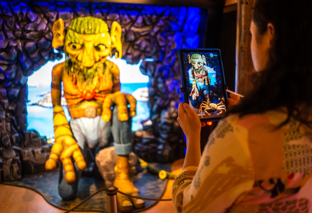 A visitor using a tablet beside a sea-troll figure in the Troll Museum