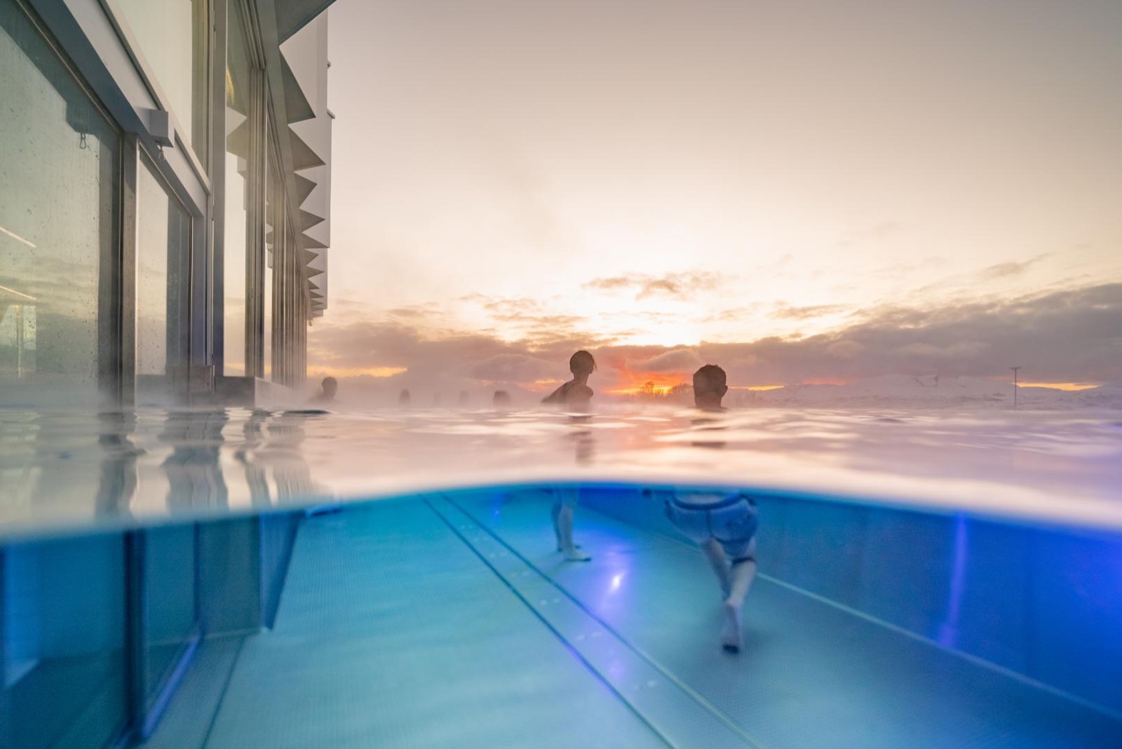 People bathing in Tromsøbadet’s heated outdoor pool with mountains beyond