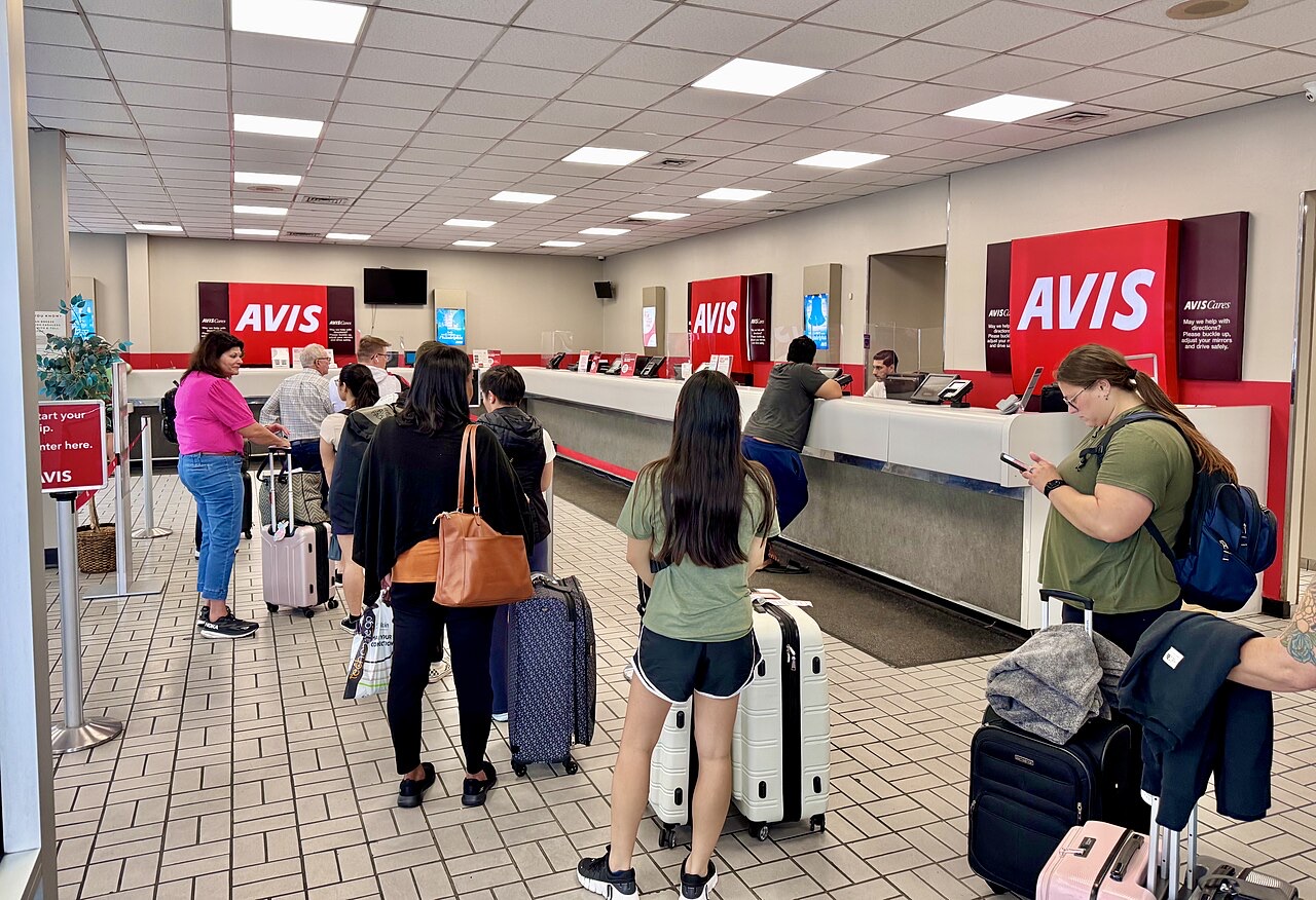 Travellers waiting at an Avis car rental counter