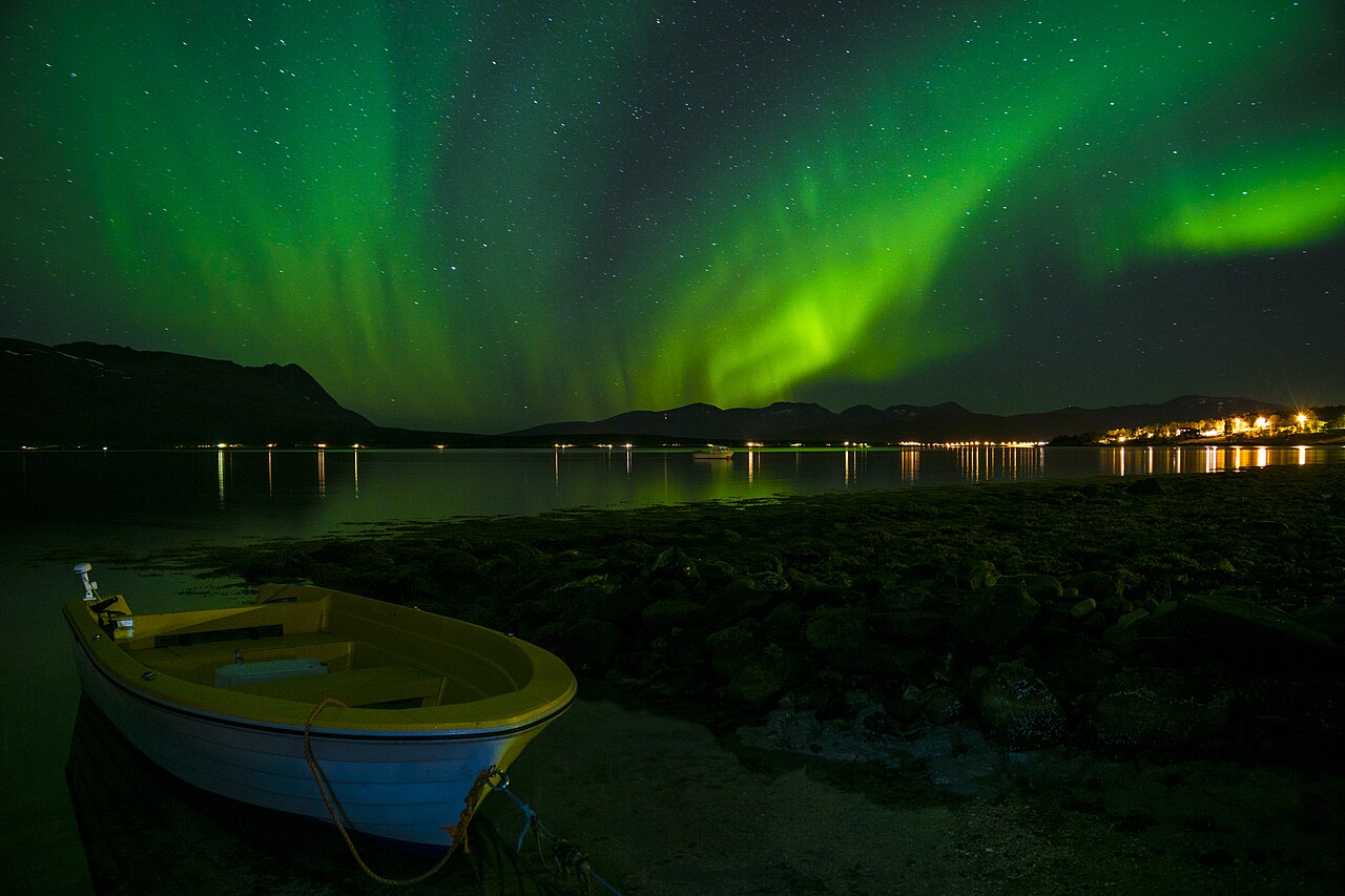 Green aurora above a shoreline and boat in the Tromsø area