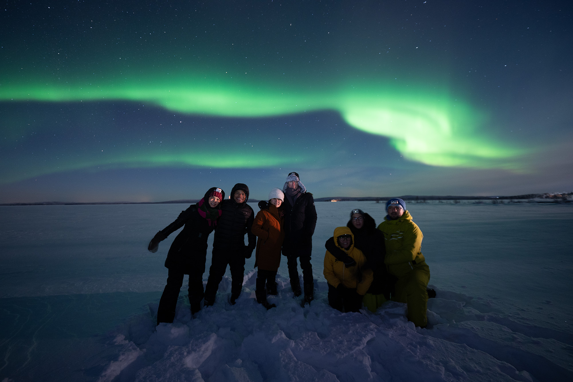 Group of travellers beneath the northern lights in a snowy landscape