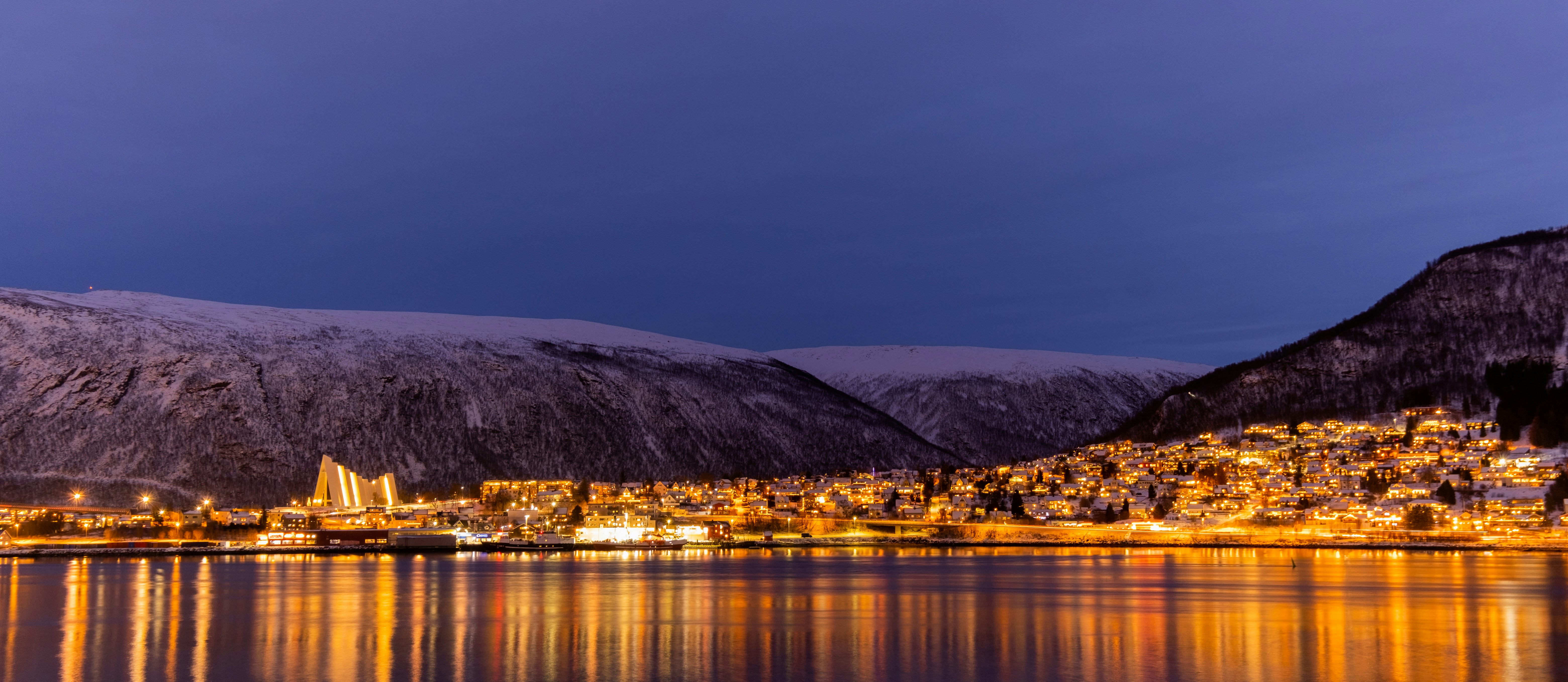 Tromsø waterfront lit against snowy mountains after dark