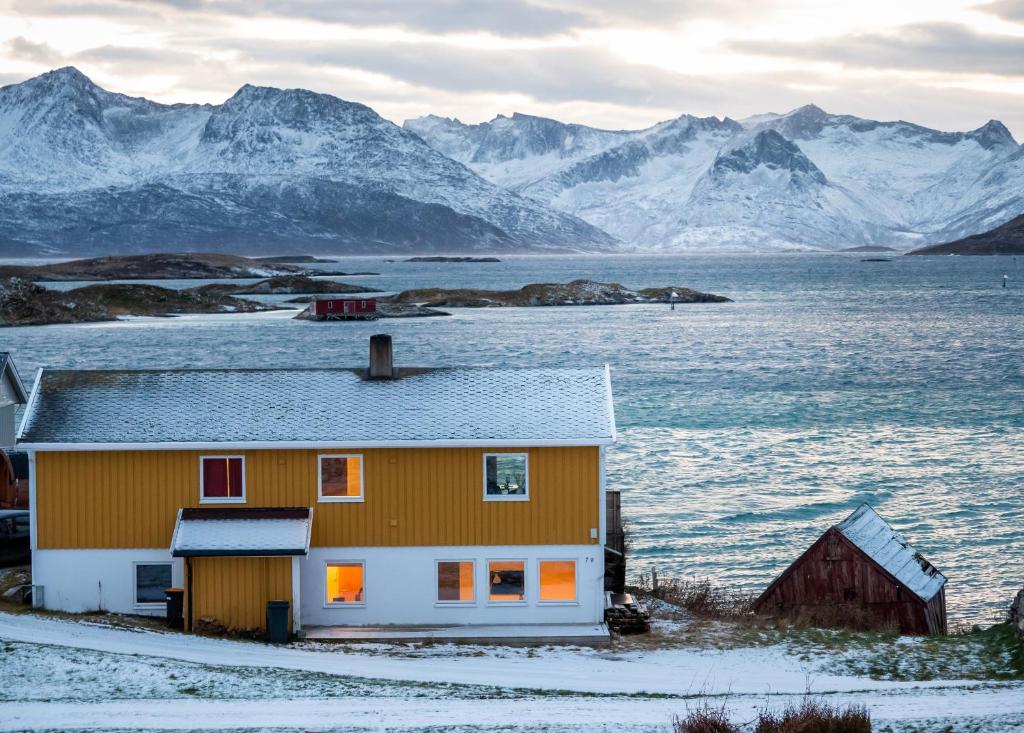 a house in the snow with mountains in the background at Sommarøya Beach Apartment in Tromsø — Sommarøya Beach Apartment