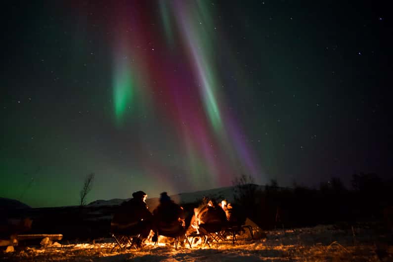 Travellers in winter clothes beneath northern lights near Tromsø